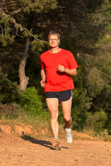 Young man running on the forest road at springtime