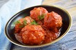 Meatballs with sauce and greens in a pan on a wooden background.