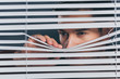 suspicious young man looking away and peeking through blinds