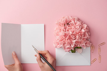 Wall Mural - cropped shot of woman writing on greeting card and pink flowers in envelope isolated on pink