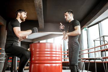 Wall Mural - Boxing trainer showing to a man how to fight, teaching to box in the boxing ring at the gym