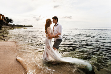 Wall Mural - Bride and groom embracing look at each other standing in the sea water on the beach