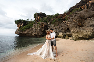 Wall Mural - Bride and groom hugging on the beach against the backdrop of rocks