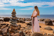 © Andzo Janovich - Young woman in long dress, in hands holds a Viking sword.Model posing on background of sea shore and zen pyramid of stones