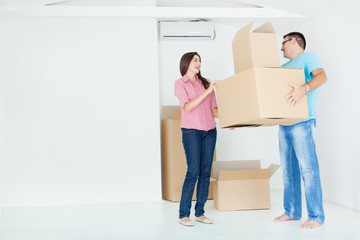 Portrait of beautiful, excited woman and man holding unpacking cardboard boxes in new home,copy space