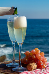 Waiter pouring Champagne, prosecco or cava in two glasses on outside terrace with sea view