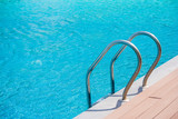 Fototapeta  - Close up grab bars ladder with blue water in swimming pool in the background. (Selective focus)