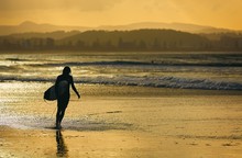 A Lone Surfer Walks The Beach Near Sunrise