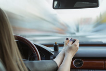 A Young Girl Is Not Driving Safely. Paints Toenails While Driving. The Concept Of Accidents, Inattention At The Wheel, The Danger To The Driver