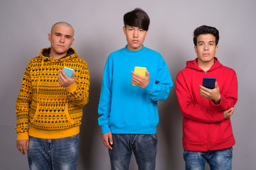 Three young Asian men wearing warm clothing against gray backgro