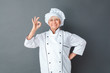© Viktoriia - Senior woman chef studio standing isolated on gray posing showing ok cheerful