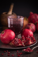 Wall Mural - Pomegranate juice in a glass on the silver tray with fresh pomegranates around with scattered seeds on dark background