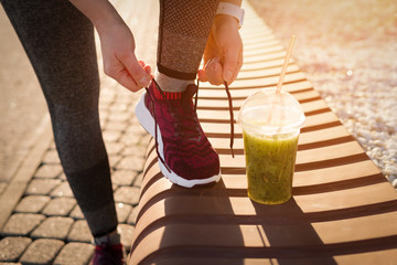 Wall Mural - Green detox smoothie cup and woman lacing shoes before workout.