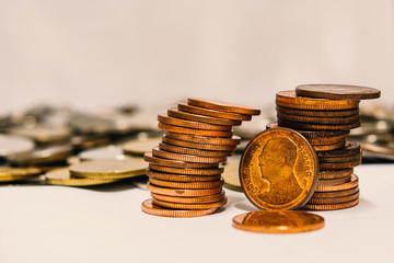 two stacks of copper coins, with a single coin in front of them. There is a blurred background of more coins.