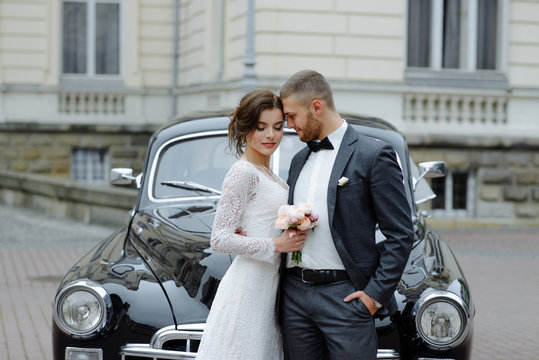elegant gorgeous bride and handsome groom embracing in stylish black car in light. unusual view from back. luxury wedding couple in retro style.