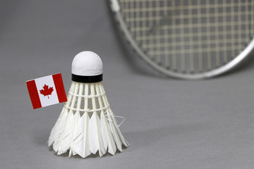 Mini Canada flag stick on the white shuttlecock on the grey background and out focus badminton racket.