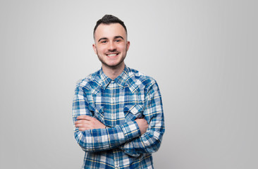 Wall Mural - Happy young guy in blue checkered shirt, is crossing hands and looking at camera