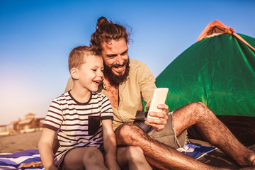 Father and son at the beach using phone and having fun