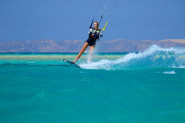 Kite surfing girl in sexy swimsuit with kite in sky on board in blue sea riding waves with water splash. Recreational activity, water sports, action, hobby and fun in summer time. Kiteboarding sport