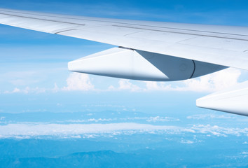 Close up airplane wing flying at blue sky in sunny day over cloud.