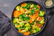 Vegan wok stir fry with broccoli and carrot in black dish.