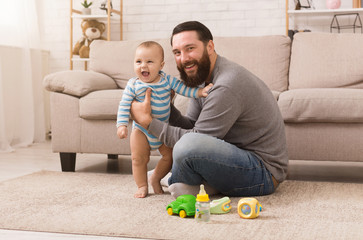 Happy father playing with his baby son with bright rattle