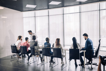 Rear view of business people sitting in a raw and listening a business coach at seminar at spacious modern conference room with panoramic windows