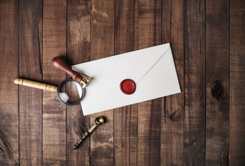 Wall Mural - Blank paper envelope with red wax seal, stamp, spoon and magnifier on wooden background. Mockup for your design. Flat lay.