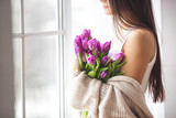 Fototapeta Tulipany - Unrecognizable young woman holding flowers indoors