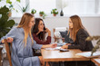 © yavdat - A group of three women are sitting in a cafe and talking about a new business. together calculate taxes or income from a business idea.