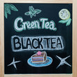 © Mariana - Blackboard with black tea and green tea inscriptions and with painted cake and lemon. Stylish concept of tea drinking, lettering