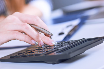 Business woman hand using a calculator with silver pen in office closeup.