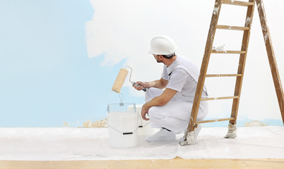 Wall Mural - painter man at work takes the color with paint roller from the bucket and look the wall, copy space template