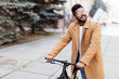 © F8  \ Suport Ukraine - Happy young indian man dressed in shirt and coat standing with a fixed gear bicycle on city street