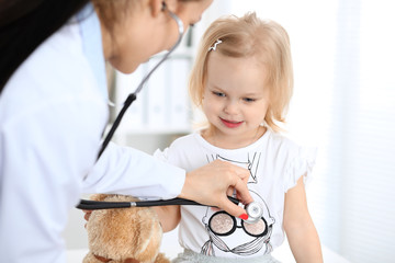 Wall Mural - Doctor and patient baby in hospital. Little girl is being examined by pediatrician with stethoscope. Health care, insurance and help concept