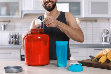 Wall Mural - Young man preparing protein shake at table in kitchen, closeup