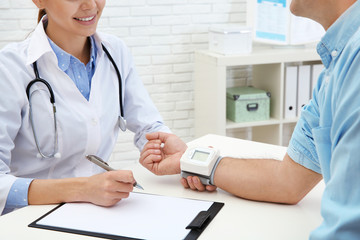 Canvas Print - Doctor checking mature man's pulse with medical device in hospital, closeup