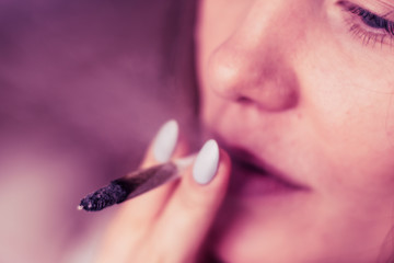 joint in woman hand. A woman smokes cannabis weed, a . Smoke on a black background. Concepts of medical marijuana use and legalization of the cannabis. On a black background Pink tinting