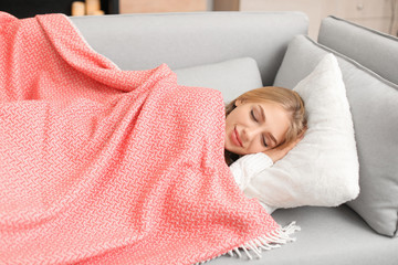 Poster - Beautiful young woman covered with plaid sleeping on sofa at home. Winter atmosphere