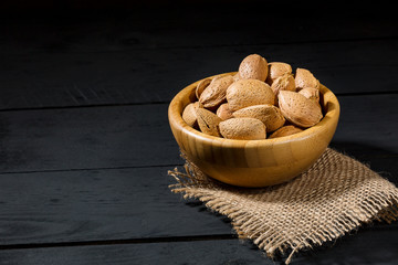 Wall Mural - Almonds with shell in wooden bowls on slate background