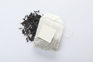 Poster - Dry tea leaves and unused bag with tag on white background, top view. Space for text