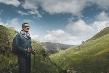 Wall Mural - Traveler Man With Backpack And Trekking Poles Resting And Looking At The Mountains In Summer Outdoor