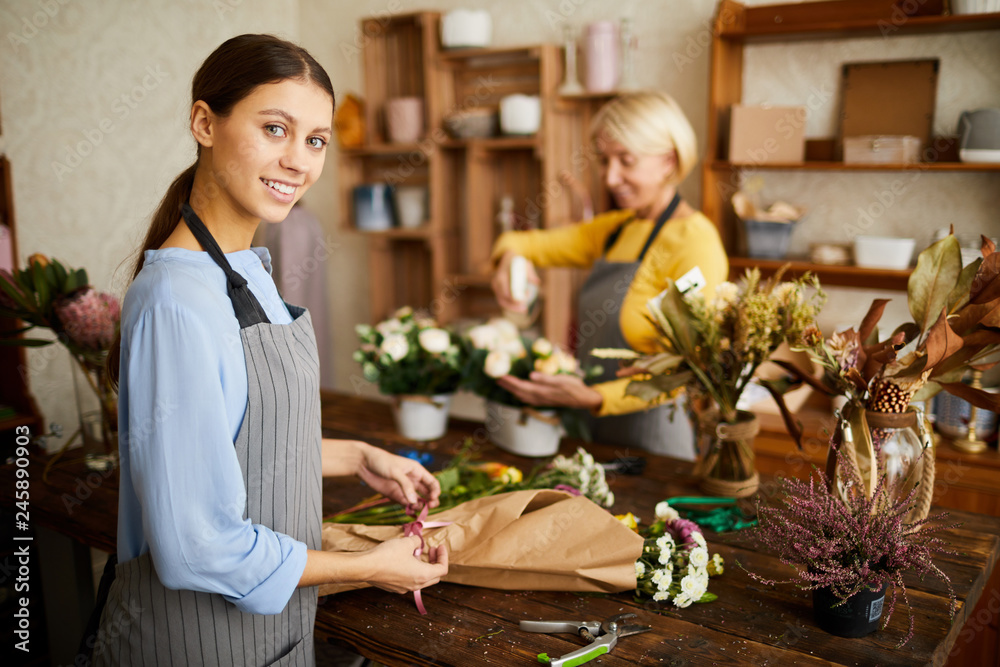 Portrait of smiling female florist cutting flower stems while arranging bouquets in flower shop, copy space - obrazy, fototapety, plakaty 