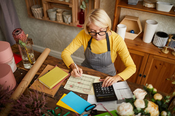 high angle portrait of female businesswoman counting finances using calculator in small shop, copy s