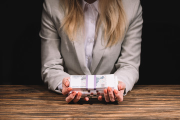 mid section of businesswoman holding russian rubles banknotes at wooden table on black