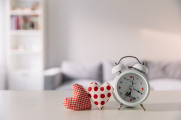 Valentines day concept. Hand make yarn red heart and white alarm clock on table and bright room background in Valentines date 14 February.