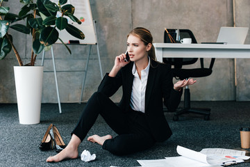 barefoot woman sitting on floor and talking on smartphone