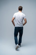 © opolja - back view of a casual young man walking and looking to side on gray background.