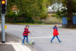 © Irina Schmidt - Two little schoolkids boys running and driving on scooter on autumn day. Happy children in colorful clothes and city traffic crossing pedestrian crosswalk with traffic lights.
