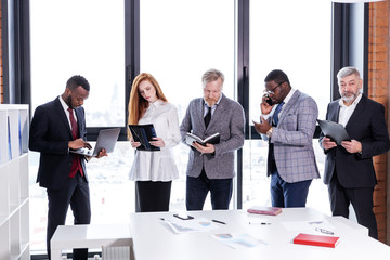 Business team of ethnic people working in the office standing at the table holding notebooks